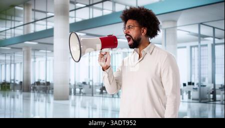Der aufgeregte Afroamerikaner meldet Nachrichten mit Lautsprecher im Büro. Stockfoto