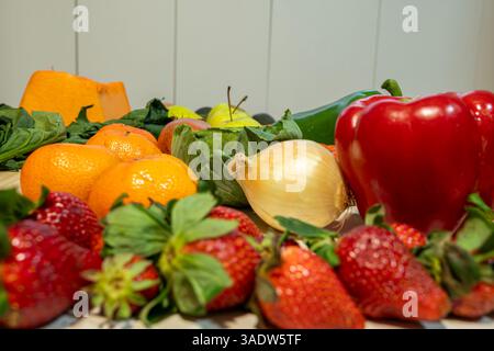 Eine Vielzahl von Obst und Gemüse wird auf einem Tisch angezeigt, darunter Äpfel, Orangen, Erdbeeren und Paprika. Stockfoto