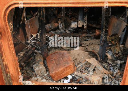 Verbrannte und zerstörte die verrostete Kabine eines gepanzerten Militärfahrzeugs. Rostiger Benzinkanister liegt auf Brandruinen in schwarzem Ruß im gepanzerten Personal c Stockfoto