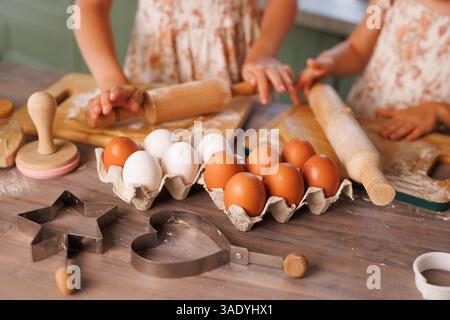 Kinder backen gemeinsam Kekse, Rollen Teig und verwenden Cutters mit frischen Eiern und Mehl auf einem rustikalen Tisch. Stockfoto