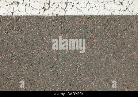 Asphaltoberfläche, Hintergrund. Ein alter Asphalt mit einem weißen Streifen, der mit Straßenfarbe aufgetragen wurde. Straßenhintergrund mit weißem Streifen oben. Detaillierte Textur Stockfoto