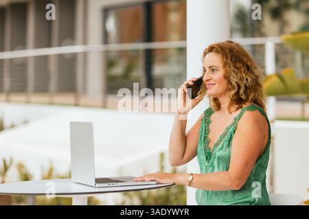 Frau, die von der Hotelterrasse aus arbeitet, während sie einen Anruf entgegennimmt. Feiertage. Lifestyle. Stockfoto