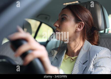 Ein hübsches Mädchen im Business-Anzug, das Auto fährt, schaut auf ihre Uhr und wird nervös. Stress während der Fahrt, Warten im Stau, Mädchen kommt zu spät für den AA Stockfoto
