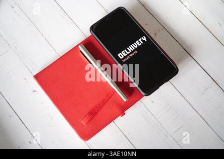 Mobiltelefon mit App-Bildschirm für E-Commerce-Logistik-Startup Delhivery, das auf rotem Tagebuch sitzt und Geschäftsabschlüsse zeigt Stockfoto