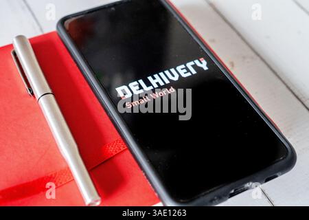 Mobiltelefon mit App-Bildschirm für E-Commerce-Logistik-Startup Delhivery, das auf rotem Tagebuch sitzt und Geschäftsabschlüsse zeigt Stockfoto