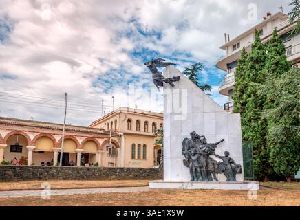 Das griechische Flüchtlingsgedenkmal in Xanthi, Thrakien, Griechenland. Das alte Gebäude des überdachten Stadtmarktes befindet sich im Hintergrund. Stockfoto