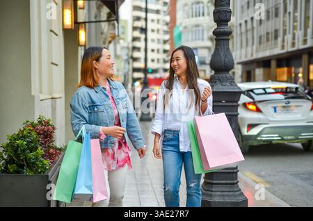Zwei Frauen, die die Straße hinunter laufen, Einkaufstaschen tragen und ihre gemeinsame Zeit genießen Stockfoto