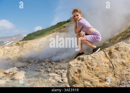 Das Modemodell der Frau sitzt mit geschlossenen Augen auf einem großen Felsen im Krater eines aktiven Vulkans und genießt Naturgeräusche, entspannt und Stockfoto