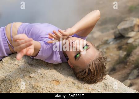 Authentizität Frau Mode Model mit geschlossenen Augen auf dem Rücken auf einem großen Felsen im Krater eines aktiven Vulkans und streckt ihre Arme vor ihr. Stockfoto