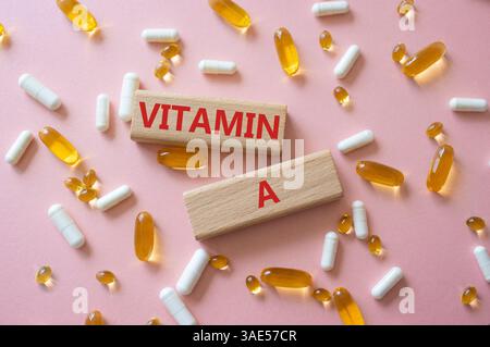 Vitamin-A-Symbol. Konzeptwort Vitamin A auf Holzblöcken. Schöner rosafarbener Hintergrund mit Pillen. Medizin und Vitamin-A-Konzept. Kopierbereich Stockfoto