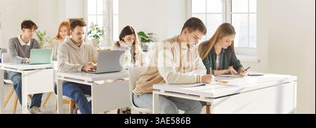 Gruppe von Studenten oder Schülern der High School, die an Schreibtischen mit Laptops sitzen und im Klassenzimmer studieren Stockfoto