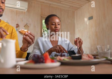 Zwei Freunde, ein junger afroamerikanischer Mann und eine Frau im Resort-Urlaub, plaudern sich entspannt und genießen gemeinsam Frühstück. Stockfoto