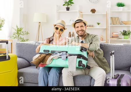 Positives Familienpaar, das mit gepacktem Koffer auf dem Sofa im Wohnzimmer sitzt Stockfoto