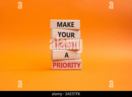 Gesundheitssymbol. Holzblöcke mit Worten machen Ihre Gesundheit zu einer Priorität. Wunderschöner orangefarbener Hintergrund. Gesundheitskonzept. Kopierbereich. Stockfoto