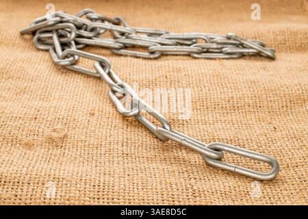 Ein Stück Metallkette auf Jute-Tuch, Makro. Stockfoto