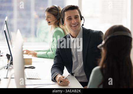 Zufriedene Callcenter-Kollegen, die Headsets tragen und am Arbeitsplatz sprechen Stockfoto
