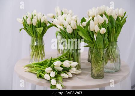 Ein Tisch mit verschiedenen Vasen gefüllt mit weißen Tulpen. Die Vasen sind in einer Reihe angeordnet, wobei einige größer und andere kürzer sind. Die Szene ist eine von Eleganz Stockfoto