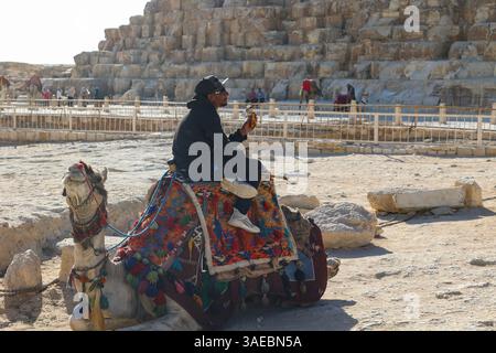 Ein arabischer Mann sitzt auf einem dekorierten Kamel mit Eis in der Hand unter der großen ägyptischen Pyramide Stockfoto