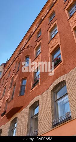 Fassade eines historischen europäischen Gebäudes mit kunstvollen architektonischen Details, Blumenkästen und strukturierten orangen Wänden unter klarem blauen Himmel. Stockfoto