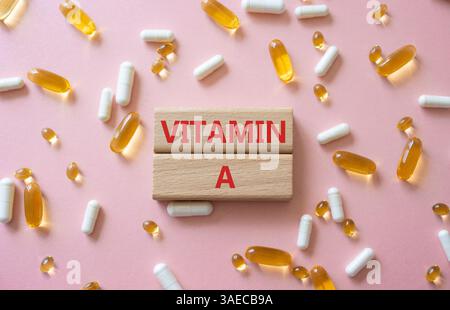Vitamin-A-Symbol. Konzeptwort Vitamin A auf Holzblöcken. Schöner rosafarbener Hintergrund mit Pillen. Medizin und Vitamin-A-Konzept. Kopierbereich Stockfoto