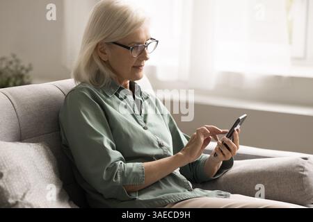 Porträt glückliche ältere Frau, die auf der Couch sitzt und auf dem Smartphone SMS schreibt Stockfoto