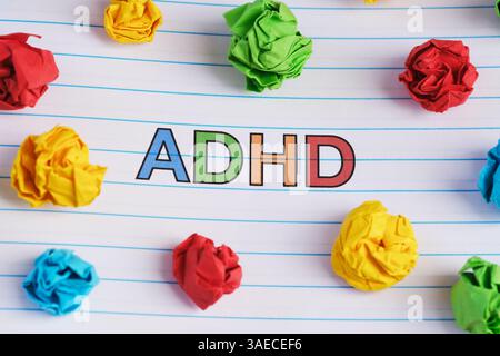 ADHS. Die Abkürzung ADHD steht auf einem Notizblock mit bunten zerknitterten Papierkugeln. Nahaufnahme. Stockfoto