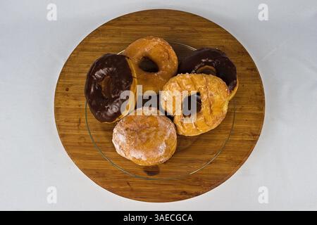 Eine Überkopfaufnahme aus verschiedenen Donuts, glasiert und mit Schokolade überzogen, angeordnet auf einem hölzernen Servierbrett auf weißem Hintergrund für eine süße Köstlichkeit. Stockfoto