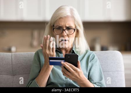 Nervöse Seniorin hält Kreditkarten auf den Bildschirm Stockfoto