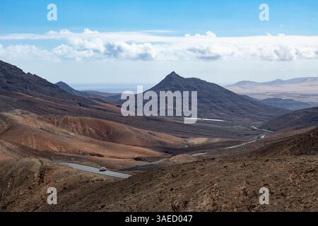Abgelegene Straße mit Auto durch das karge vulkanische Tal auf Fuerteventura Stockfoto
