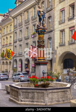 Bern, Schweiz, 20. Mai 2024. Dieser farbenfrohe historische Brunnen steht im Herzen der Altstadt von Bern, Schweiz. Gekrönt von einer Statue von Lady Justice mit ihrer ikonischen Waage und ihrem Schwert, ist der Justice Fountain aus dem 16. Jahrhundert und eines der meistfotografierten Wahrzeichen der Stadt. Die Basis umgibt leuchtende rote Geranien, während über ihnen kräftige Fahnen flattern und dem zeitlosen Steinplatz eine festliche Energie verleihen. Eine perfekte Mischung aus mittelalterlichem Symbolismus und urbanem Charme. Stockfoto