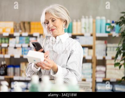 Ältere Frau in Sommerkleidung scannt den Code auf der Packung der Pillen, um das Verfallsdatum zu überprüfen Stockfoto