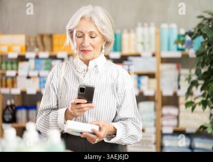 Ältere Frau in Sommerkleidung scannt den Code auf der Packung der Salbe, um das Verfallsdatum zu überprüfen Stockfoto