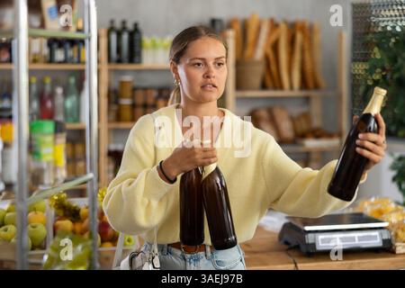 Die Käuferin untersucht Bierflaschen, wählt den richtigen Hersteller, nimmt verschiedene Flaschen aus dem Regal. Stockfoto