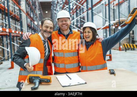 Lagerarbeiter und ihre Manager umarmen sich gegenseitig und feiern einen erfolgreichen Logistikbetrieb in einem großen Vertriebszentrum Stockfoto
