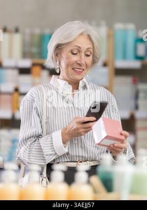 Ältere Frau in Sommerkleidung scannt den Code auf der Packung der Pillen, um das Verfallsdatum zu überprüfen Stockfoto