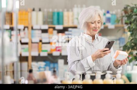 Ältere Frau in Sommerkleidung scannt den Code auf der Packung der Pillen, um das Verfallsdatum zu überprüfen Stockfoto