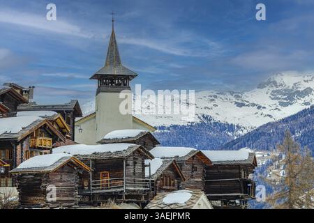 Alte Holzhäuser mit schneebedeckten Dächern und die Kirche Saint Theodule im historischen Dorfkern Grimentz, Val d'Anniviers, Walliser Alpen, Kanton Stockfoto