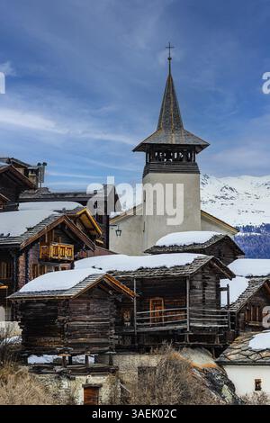 Alte Holzhäuser mit schneebedeckten Dächern und die Kirche Saint Theodule im historischen Dorfkern Grimentz, Val d'Anniviers, Walliser Alpen, Kanton Stockfoto