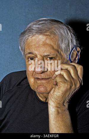 Dramatisches Seitenporträt eines älteren Mannes mit einer Brille in der Hand neben seinem Gesicht in einem schwarzen Hemd isoliert auf grau/blau, New York, USA Stockfoto