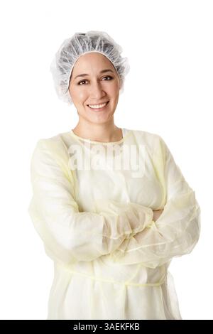 Glückliche lächelnde medizinische Assistentin für ein chirurgisches Team oder Zahnarzt mit gelben Peelings und weißem Haarnetz stehend mit gekreuzten Armen, isoliert, N Stockfoto