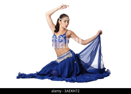 Schöne israelische ägyptische libanesische Bauchtänzerin aus dem Nahen Osten in blauem Rock und BH mit Arm in Luft sitzend mit geschlossenen Augen, isoliert, ne Stockfoto