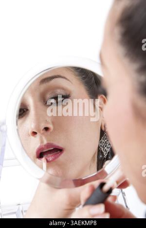 Schöne weiße Frau, die Make-up Lippenstift auf die Lippe aufträgt, während sie in Handspiegel blickt, isoliert, New York, USA, Nordamerika Stockfoto