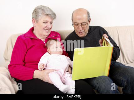 Gerne Spaß kaukasischen Hispanic im Nahen und Mittleren Osten Familie zusammen auf der Couch lesen Buch sitzen zum Baby. Großvater und Großmutter lesen grüne Buch i Stockfoto