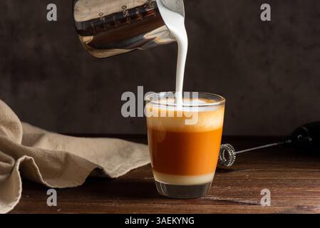 Heißer Thai Tee Latte mit Milchschaum im Glas. Milchschaum in das Glas gießen. Stockfoto