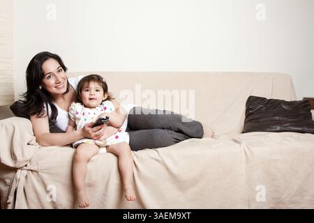 Schöne glückliche Familienmutter und kleine Tochter sitzen entspannt auf der Couch im Wohnzimmer und schauen Fernsehen, New York, USA, N Stockfoto