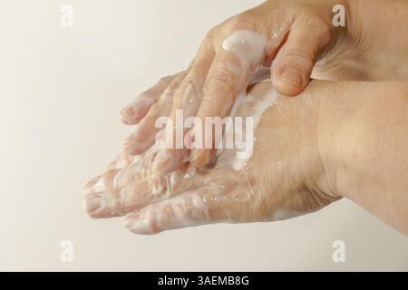 Nahaufnahme einer Frau, die eine weiße Creme an ihren Händen reibt Stockfoto
