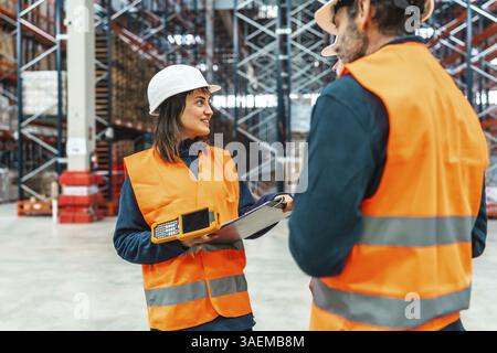 Zwei Lagerarbeiter diskutieren über Logistik, halten einen Handscanner und eine Zwischenablage in der Hand und verbessern so die Effizienz und Organisation in der Lieferkette Stockfoto
