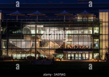 Modernes Glasgebäude in der Nacht mit Leuten, die sich im Inneren versammelten Stockfoto