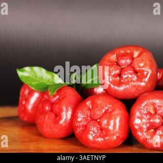 Eine lebendige Ansammlung reifer Rosenäpfel, frisch gepflückt und auf einer rustikalen Holzoberfläche ausgestellt. Stockfoto