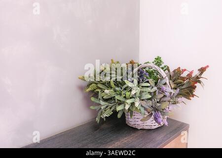 Ein Korb mit Blumen sitzt auf einem Holztisch. Die Blumen sind eine Mischung aus verschiedenen Farben und Arten, die eine lebendige und lebhafte Atmosphäre schaffen. Den Korb Stockfoto
